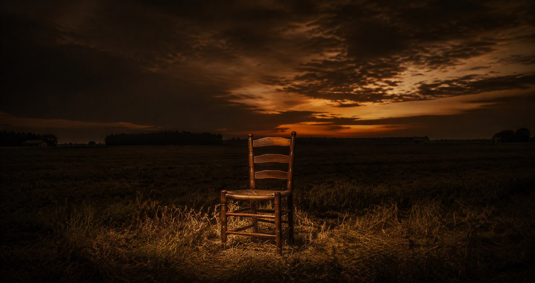 A single empty chair in a Maryland field at dusk, lit by a warm spotlight under a dark sky